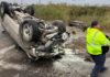 Flipped car, wheels up in the air, with a transportation worker on the scene