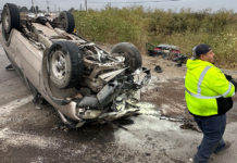 Flipped car, wheels up in the air, with a transportation worker on the scene