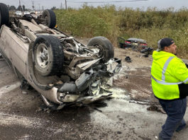 Flipped car, wheels up in the air, with a transportation worker on the scene