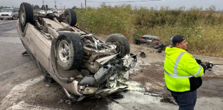Flipped car, wheels up in the air, with a transportation worker on the scene
