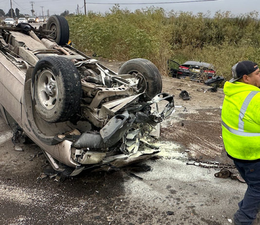 Flipped car, wheels up in the air, with a transportation worker on the scene