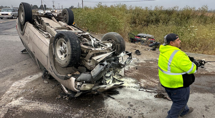 Flipped car, wheels up in the air, with a transportation worker on the scene