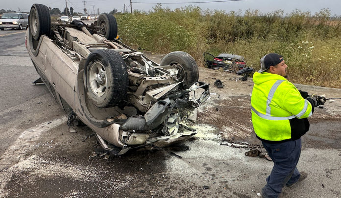 Flipped car, wheels up in the air, with a transportation worker on the scene