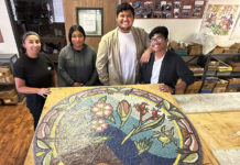 Four young people standing behind a round mosaic artwork