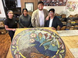 Four young people standing behind a round mosaic artwork