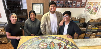 Four young people standing behind a round mosaic artwork