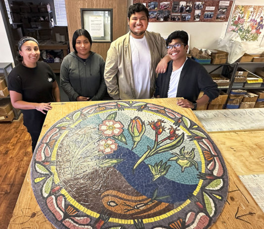 Four young people standing behind a round mosaic artwork