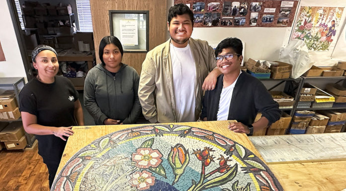 Four young people standing behind a round mosaic artwork