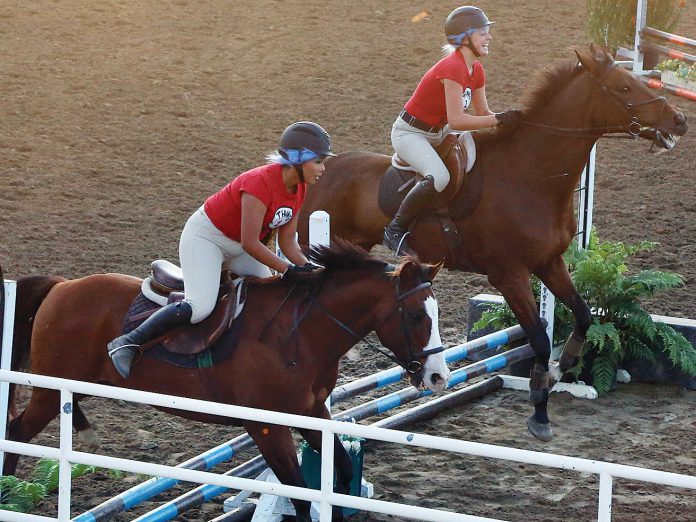 horses These women take part in the pair jumping competition in the horse arena.
