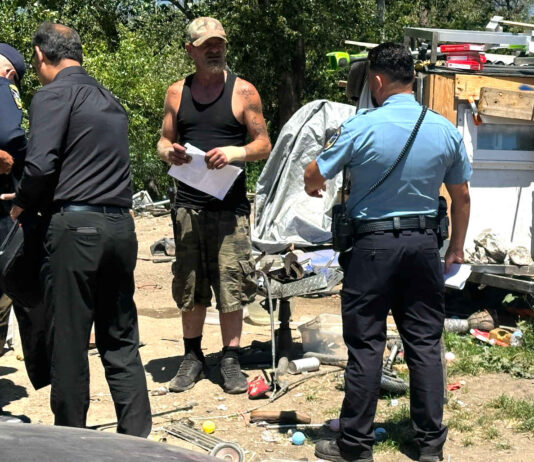 A “Notice To Vacate” flier is handed to Edward Lovell Thursday where he lives at a homeless encampment on Airport Boulevard.