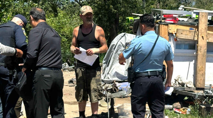 A “Notice To Vacate” flier is handed to Edward Lovell Thursday where he lives at a homeless encampment on Airport Boulevard.