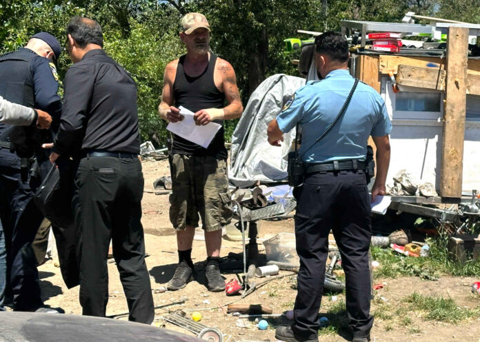 A “Notice To Vacate” flier is handed to Edward Lovell Thursday where he lives at a homeless encampment on Airport Boulevard.
